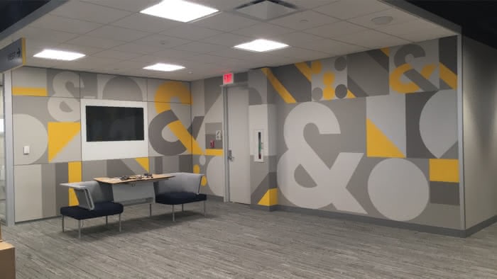 sitting area with a mural on the wall featuring a combination of grey and brand yellow in various shapes